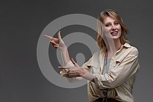 Beautiful smiling woman pointing with both hands to copyspace on her left hand side against a grey studio background