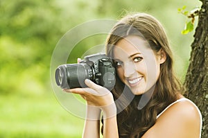 Beautiful smiling woman is professional photographer with DSLR camera and taking pictures outdoors in summer nature.