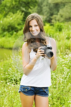 Beautiful smiling woman is professional photographer with DSLR camera and taking pictures outdoors in summer nature