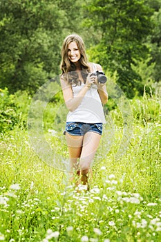 Beautiful smiling woman is professional photographer with DSLR camera and taking pictures outdoors in summer nature