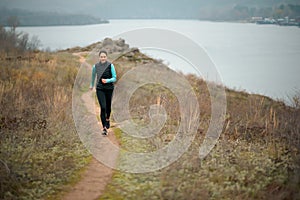 Beautiful Smiling Woman Running on the Mountain Trail at Cold Autumn Evening. Sport and Active Lifestyle