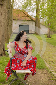 Beautiful smiling woman sitting on a bench in a red dress with blue flowers