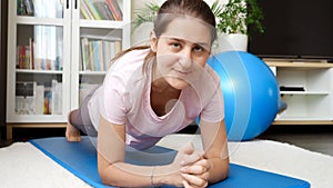 Beautiful smiling woman standing in plank and looking in camera. Concept of healthcare, sports and yoga at home