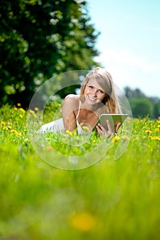 Beautiful smiling woman with tablet pc, outdoors. Beautiful young girl lying on the grass in the field. Smiling trendy stylish