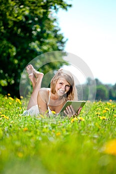 Beautiful smiling woman with tablet pc, outdoors. Beautiful young girl lying on the grass in the field. Smiling trendy stylish