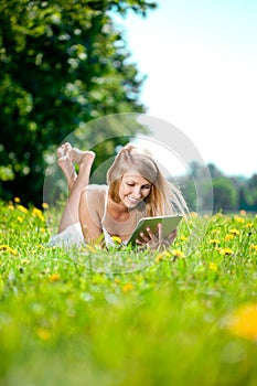 Beautiful smiling woman with tablet pc, outdoors. Beautiful young girl lying on the grass in the field. Smiling trendy stylish