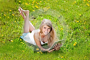 Beautiful smiling woman with tablet pc, outdoors. Beautiful young girl lying on the grass in the field. Smiling trendy stylish