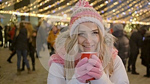 Beautiful smiling woman in warm clothing with red cup of hot tea or coffee