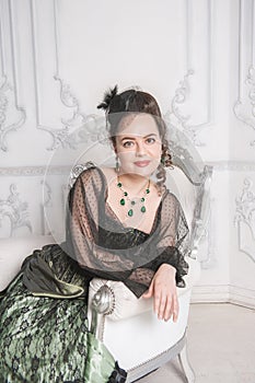 Beautiful smiling woman wearing green medieval vintage Victorian Style dress sitting in the armchair