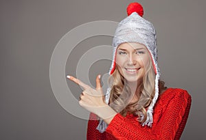 Beautiful smiling woman in winter clothing. Pointing on copyspace.