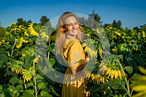 beautiful smiling woman in yellow dress looks into the camera in sunflower field