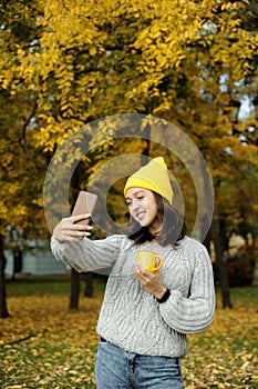 Beautiful smiling woman in yellow hat holding a cup in autumn park.