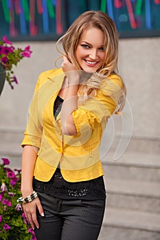 Beautiful smiling woman with yellow jacket and blond hair posing outdoor. Fashion girl