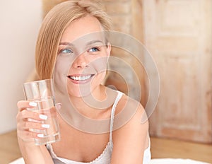 Beautiful smiling young blonde woman waking up and drinking water in the morning