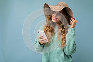 Beautiful smiling young blonde woman wearing blue sweater and hat standing isolated over blue background surfing on the
