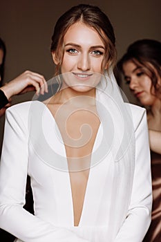 beautiful smiling young bride in long white satin dress with deep neckline, hairstyle and make up standing in hotel room