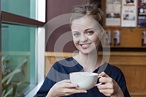 Beautiful smiling young caucasian woman girl holding white cup of coffee in a cafe, restaurant