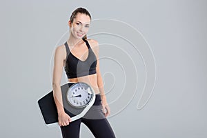 Beautiful smiling young fitness woman in tracksuit holding weigh scale