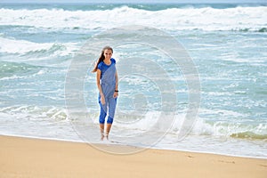 Beautiful smiling young girl in blue walking on the beach on vacation