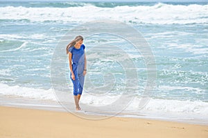 Beautiful smiling young girl in blue walking on the beach on vacation