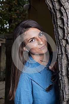 Beautiful smiling young girl with braces leaning against a tree with copy space on black background