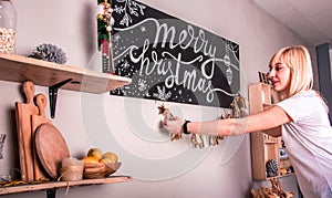 Beautiful smiling young girl hangs glitter decorations around poster with Merry Christmas inscription