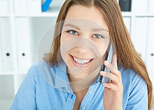 Beautiful smiling young Caucasian girl talking on the mobile phone in the office.