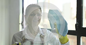 Beautiful smiling young housewife is doing household chores and washing windows