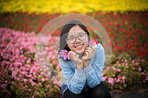 Beautiful smiling young lady holding petals squats at flower garden.