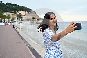 Beautiful smiling young mixed race woman takes selfie with a smartphone at the Promenade des Anglais in Nice, France