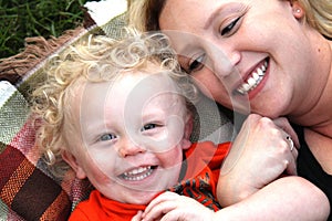 Beautiful, smiling young mother and son link arms laying on blanket.