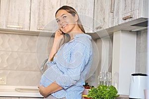 Beautiful smiling young pregnant woman at home kitchen