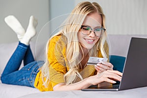 beautiful smiling young woman in eyeglasses holding credit card and using laptop