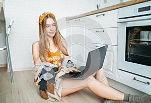 Beautiful smiling young woman fair long hair girl wearing in cozy knitted cardigan working on laptop at bright kitchen, online