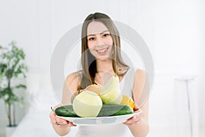 Beautiful smiling young woman holding a plate of fresh fruits, apple, pear, lemon, grapefruit, kiwi and cucumber