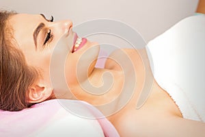 A beautiful smiling young woman is lying on a massage couch waiting for a massage in a massage room.