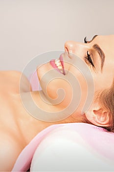 A beautiful smiling young woman is lying on a massage couch waiting for a massage in a massage room.