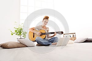 Beautiful smiling young woman playing guitar with computer, lear