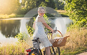 Beautiful smiling young woman posing on vintage bicycle in field at susnet