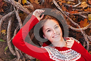 Beautiful smiling young woman in a red sweater lies in the autumn park. Top view