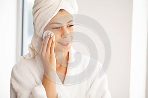 Beautiful smiling young woman removing makeup with a facial wipe