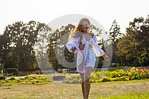 Beautiful smiling young woman runs in white clothes in a meadow with a flowers at sunset