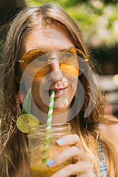 beautiful smiling young woman in sunglasses drinking tropical cocktail