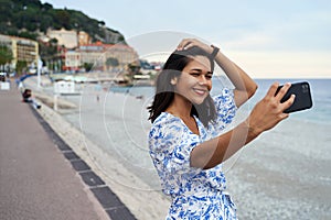 Beautiful smiling young woman takes selfie at the Promenade des Anglais in Nice, France