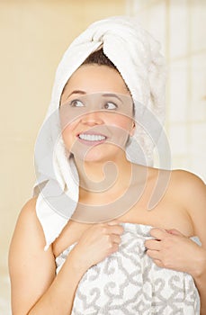 Beautiful smiling young woman with a white towel covering her head is holding with both hands her body towel
