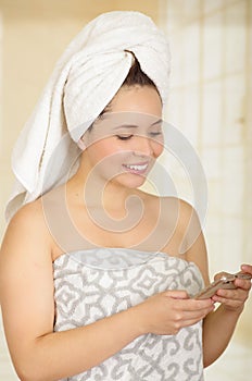 Beautiful smiling young woman with a white towel covering her head is using her cellphone