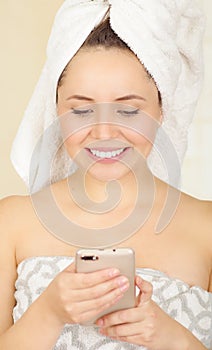 Beautiful smiling young woman with a white towel covering her head is using her cellphone