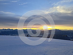 Beautiful snow-covered ski slope illuminated by warm sunset light with majestic mountain peaks