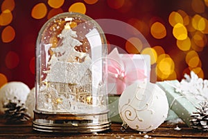 Beautiful snow globe, Christmas bauble and gifts on wooden table against blurred festive lights