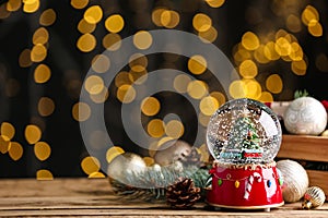 Beautiful snow globe and Christmas decor on wooden table against blurred festive lights. Space for text